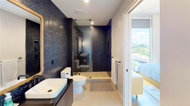 bathroom featuring tiled shower, vanity, toilet, and tile walls