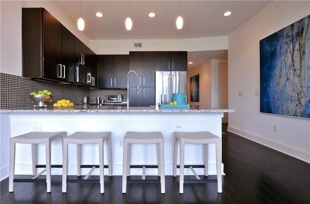 kitchen with appliances with stainless steel finishes, dark hardwood / wood-style floors, tasteful backsplash, decorative light fixtures, and kitchen peninsula