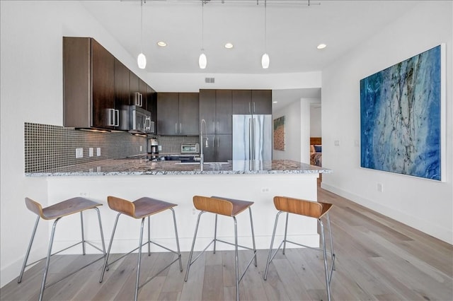 kitchen with dark brown cabinetry, decorative light fixtures, kitchen peninsula, stainless steel appliances, and decorative backsplash