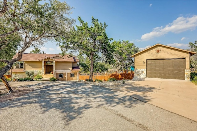 view of front of property featuring driveway, stone siding, and fence