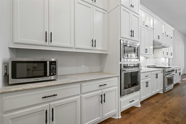 kitchen with appliances with stainless steel finishes, dark hardwood / wood-style flooring, light stone countertops, and white cabinets