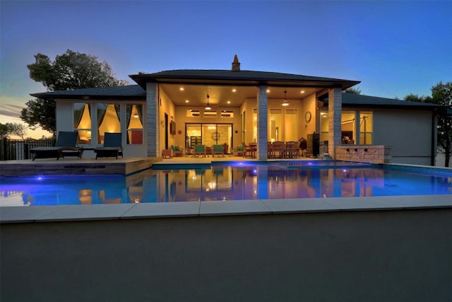 pool at dusk with a patio area and ceiling fan