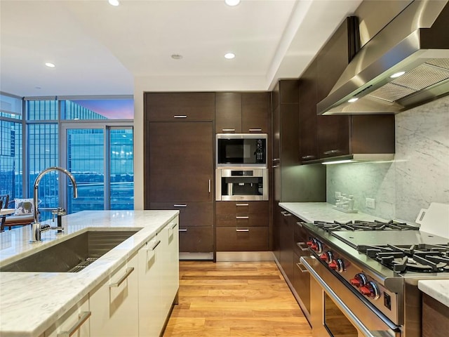 kitchen featuring ventilation hood, sink, light hardwood / wood-style floors, stainless steel appliances, and light stone countertops