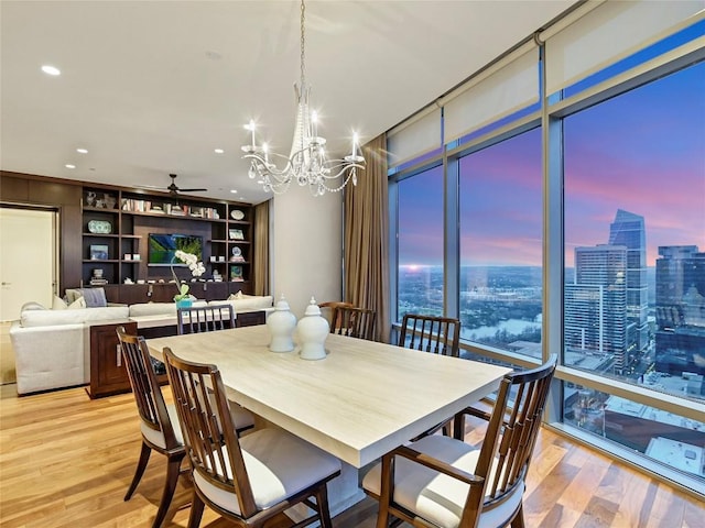 dining space featuring ceiling fan with notable chandelier, floor to ceiling windows, built in shelves, and light wood-type flooring