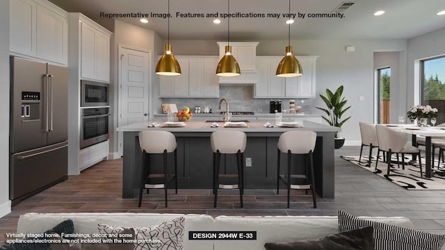 kitchen with hanging light fixtures, an island with sink, white cabinets, and appliances with stainless steel finishes