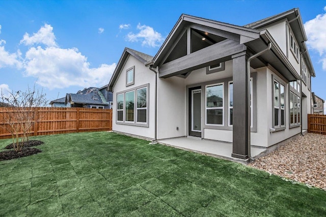 rear view of house featuring a fenced backyard, a lawn, a patio, and stucco siding