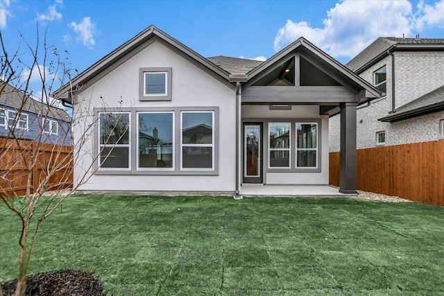 rear view of property with a yard, fence, and stucco siding