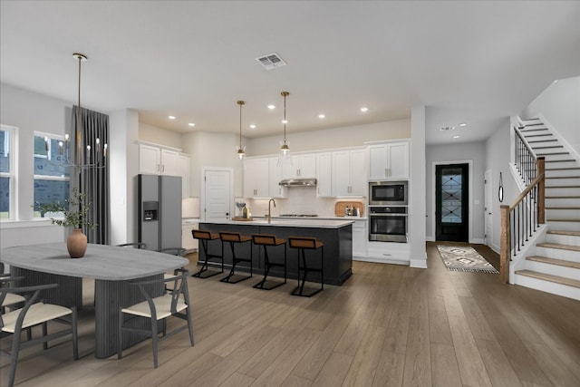 kitchen with oven, under cabinet range hood, wood finished floors, refrigerator with ice dispenser, and built in microwave