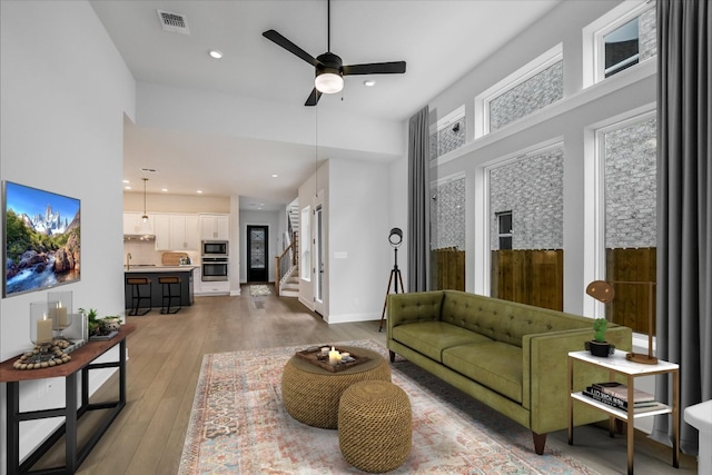 living area featuring baseboards, visible vents, stairs, light wood-style floors, and recessed lighting