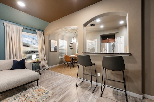 interior space featuring vaulted ceiling, light wood-type flooring, stainless steel refrigerator, pendant lighting, and dark stone counters