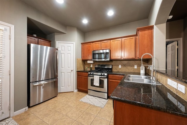 kitchen with sink, dark stone countertops, backsplash, light tile patterned floors, and stainless steel appliances