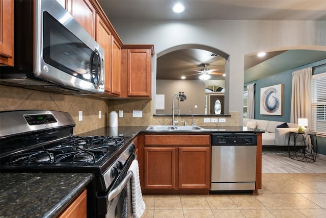 kitchen with sink, light tile patterned floors, appliances with stainless steel finishes, dark stone counters, and decorative backsplash