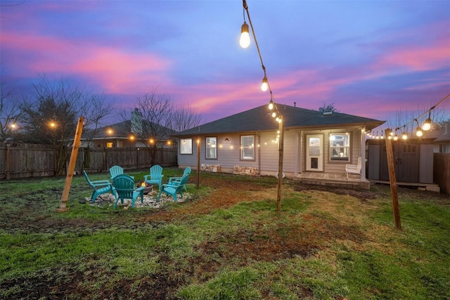 back house at dusk with an outdoor fire pit and a lawn