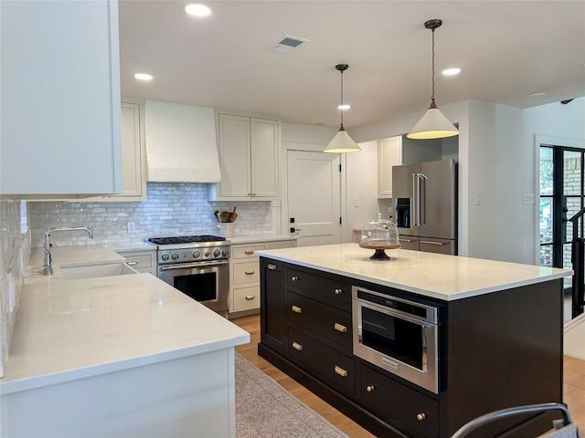 kitchen with pendant lighting, premium appliances, white cabinets, a kitchen island, and custom exhaust hood