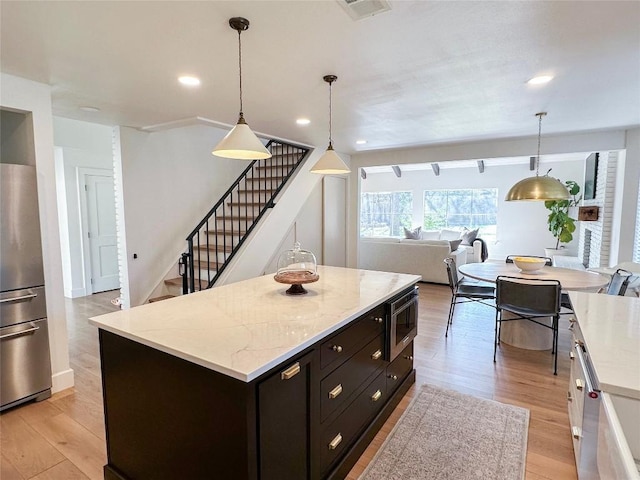 kitchen featuring pendant lighting, appliances with stainless steel finishes, a kitchen island, and light wood-type flooring