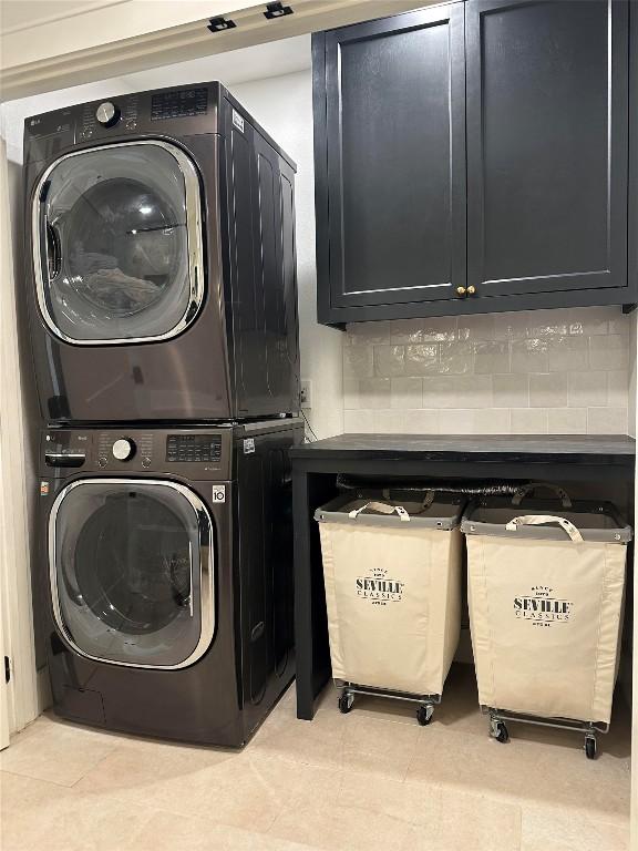 clothes washing area featuring cabinets, light tile patterned floors, and stacked washer and clothes dryer