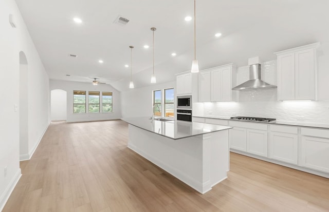 6420 Apache Plum Ln, Spicewood, TX 78669 - kitchen featuring wall chimney range hood, appliances with stainless steel finishes, arched walkways, light wood finished floors, and backsplash