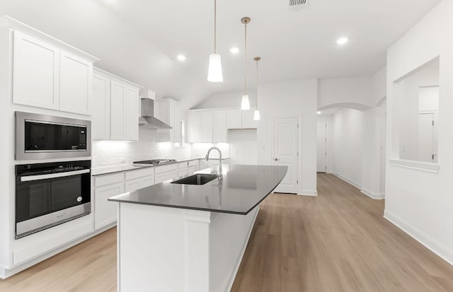 6420 Apache Plum Ln, Spicewood, TX 78669 - kitchen with stainless steel appliances, wall chimney range hood, arched walkways, a center island with sink, and light wood-type flooring