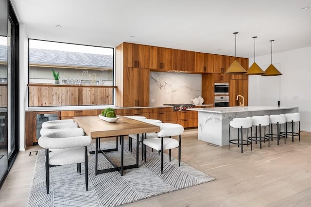 kitchen featuring a center island with sink, light wood-type flooring, pendant lighting, stainless steel appliances, and backsplash