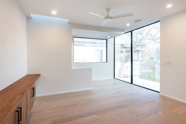 spare room featuring expansive windows, ceiling fan, a healthy amount of sunlight, and light hardwood / wood-style flooring