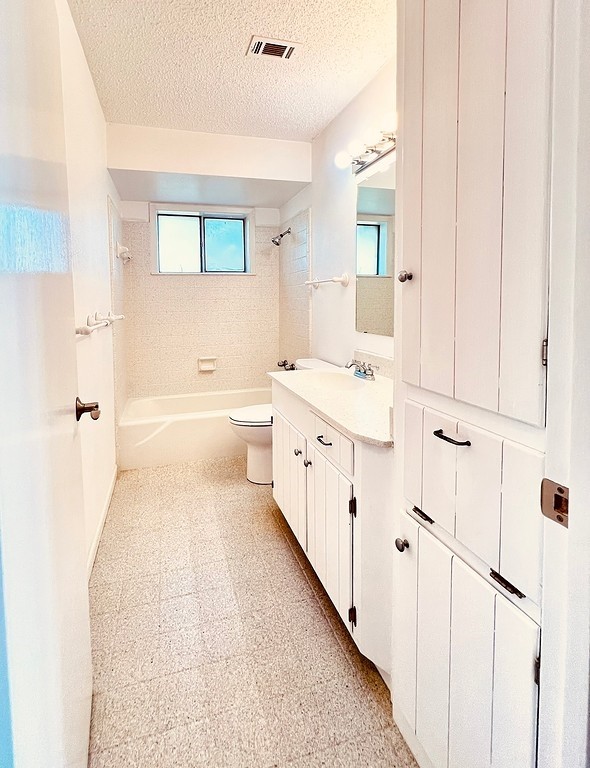 full bathroom with vanity, tiled shower / bath, toilet, and a textured ceiling