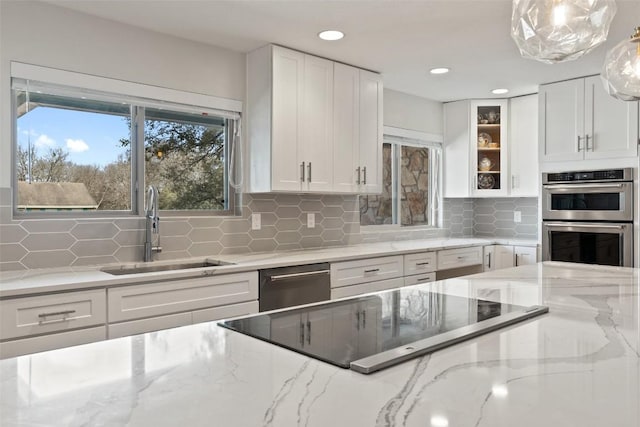 kitchen featuring pendant lighting, sink, white cabinetry, stainless steel appliances, and light stone countertops