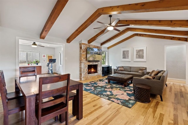 living room featuring lofted ceiling with beams, ceiling fan, a stone fireplace, and light hardwood / wood-style floors