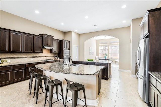 kitchen with a breakfast bar, sink, a center island with sink, appliances with stainless steel finishes, and backsplash