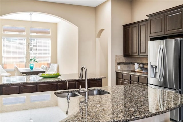 kitchen featuring stainless steel refrigerator with ice dispenser, dark brown cabinets, sink, and dark stone countertops