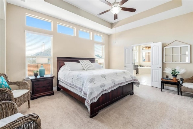 bedroom featuring a tray ceiling, ensuite bath, and light colored carpet