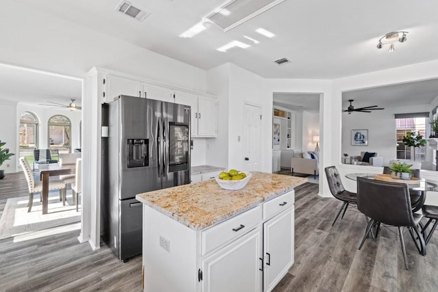 kitchen featuring stainless steel refrigerator with ice dispenser, light stone counters, a center island, hardwood / wood-style flooring, and white cabinets