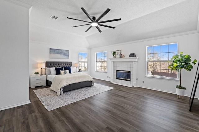 bedroom with a tiled fireplace, vaulted ceiling, dark wood-type flooring, and a textured ceiling