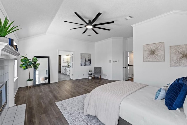 bedroom with a tiled fireplace, crown molding, dark wood-type flooring, and lofted ceiling