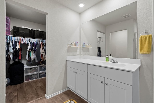 bathroom featuring visible vents, a textured wall, wood finished floors, a spacious closet, and vanity