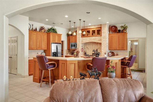 kitchen with backsplash, a kitchen breakfast bar, hanging light fixtures, light tile patterned floors, and stainless steel appliances