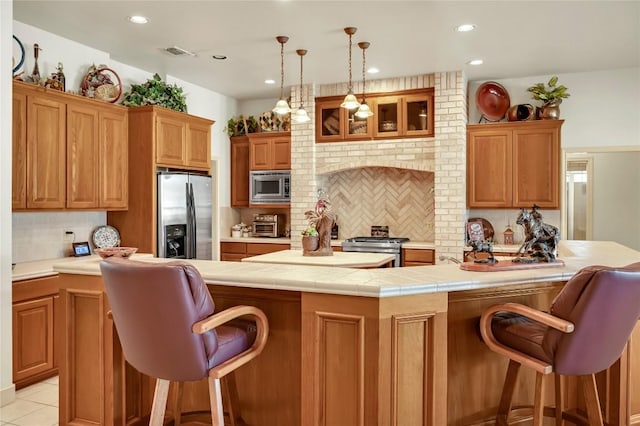 kitchen with pendant lighting, a breakfast bar area, stainless steel appliances, tile counters, and decorative backsplash