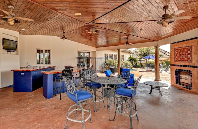 view of patio with a bar, an outdoor fireplace, and ceiling fan