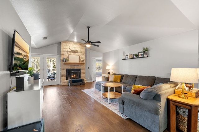 living area featuring lofted ceiling, a stone fireplace, dark wood-style flooring, and a wealth of natural light