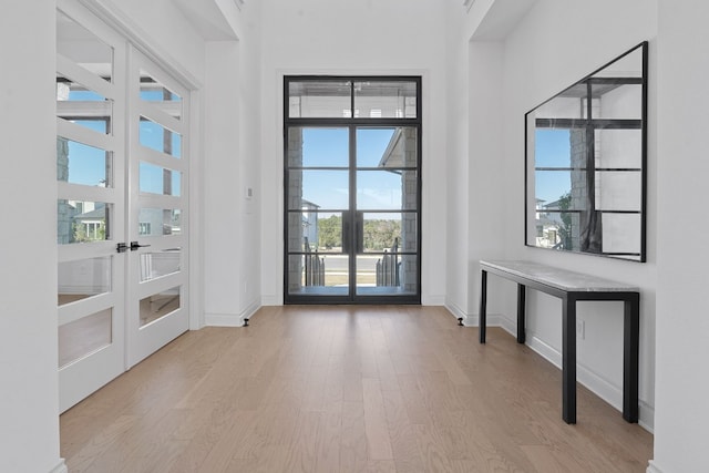 doorway with a high ceiling, light wood-type flooring, and french doors