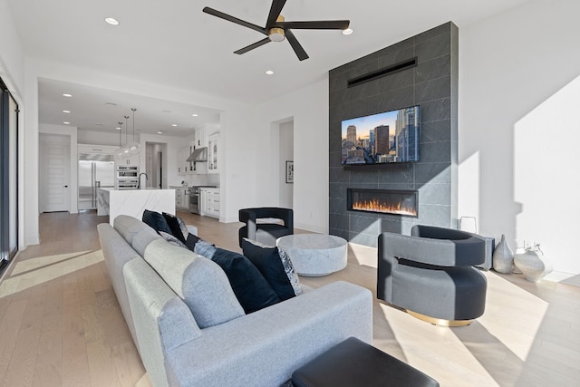 living room with a tiled fireplace, sink, ceiling fan, and light hardwood / wood-style flooring