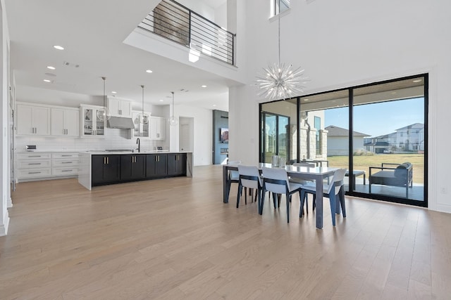 dining room featuring a towering ceiling, sink, light hardwood / wood-style floors, and a notable chandelier