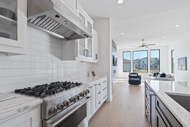 kitchen with white cabinetry, wall chimney exhaust hood, light stone counters, and high end stove