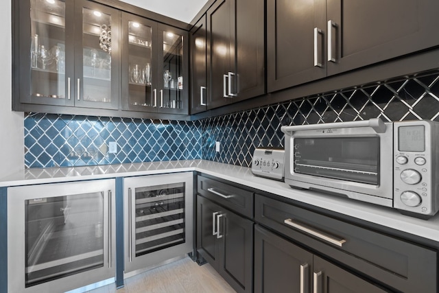 bar with wine cooler, dark brown cabinetry, and decorative backsplash