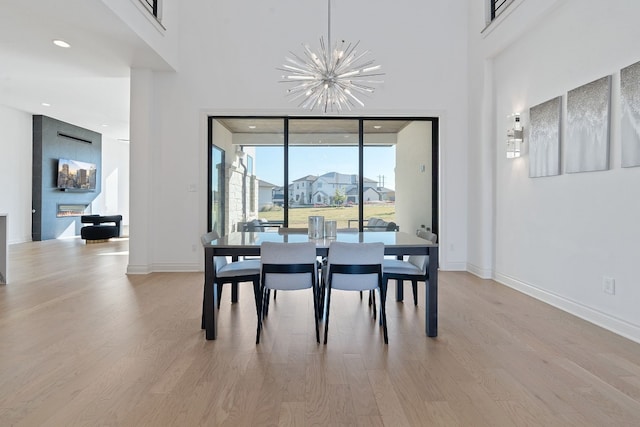 dining space with a large fireplace, a notable chandelier, light wood-type flooring, and a towering ceiling