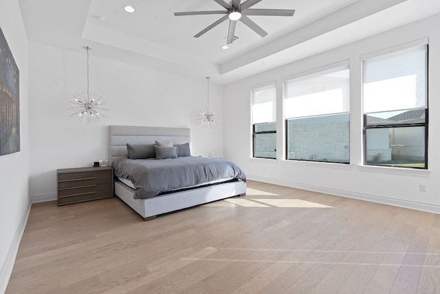 bedroom with ceiling fan with notable chandelier, light hardwood / wood-style flooring, and a tray ceiling