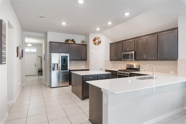 kitchen with sink, light tile patterned floors, kitchen peninsula, a kitchen island, and stainless steel appliances