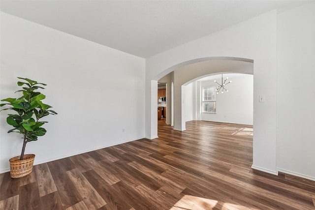 spare room with arched walkways, baseboards, dark wood-style floors, and a notable chandelier