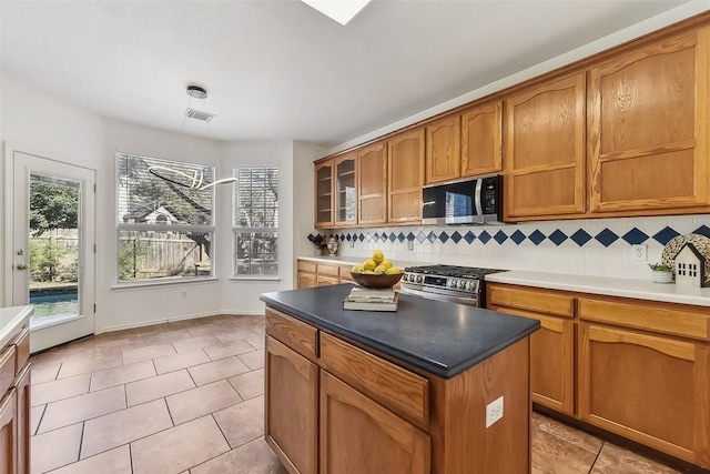 kitchen featuring brown cabinets, stainless steel appliances, visible vents, decorative backsplash, and glass insert cabinets