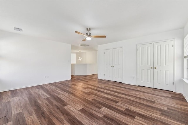 unfurnished bedroom featuring wood finished floors, visible vents, two closets, and ceiling fan