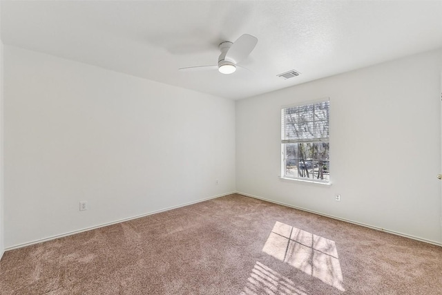 carpeted spare room featuring baseboards, visible vents, and ceiling fan